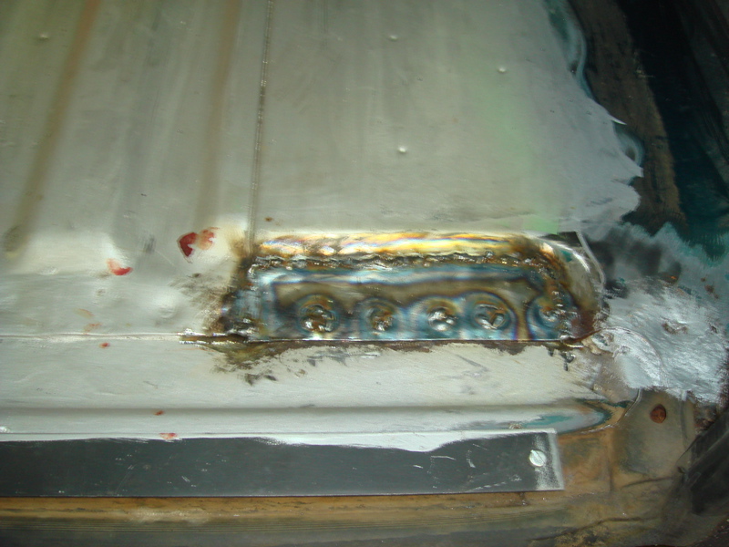 Welded metal patch on vehicle floor with visible weld marks and some red staining