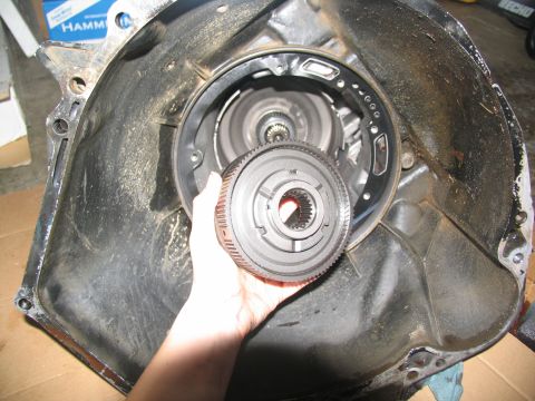 1978 Ford Bronco - A hand holds a transmission torque converter clutch in front of the transmission housing, likely during a tear-down or repair process.