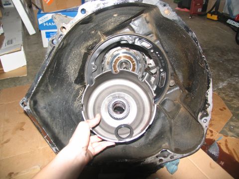1978 Ford Bronco - A hand holds a torque converter in front of a disassembled transmission bell housing.