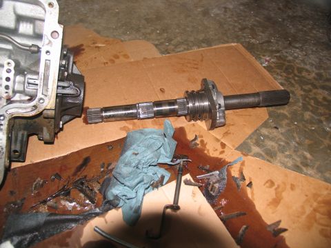 1978 Ford Bronco - Disassembled transmission components laid out on cardboard, showing a shaft and part of the casing with a fluid spill.