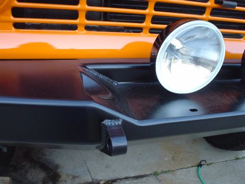 1977 Ford Bronco - Close-up of the front bumper and grille of an orange vehicle with an auxiliary light.
