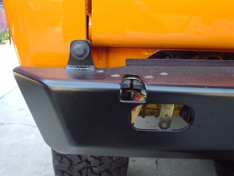 1977 Ford Bronco - The rear bumper of an orange vehicle shows a black textured finish and a visible tow hitch receiver.