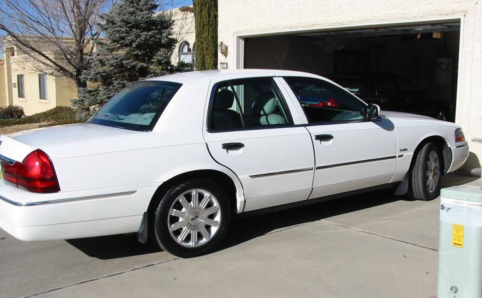 White four-door sedan with chrome wheels parked in driveway by an open garage