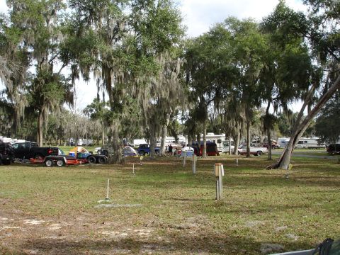 1989 Ford Bronco - A busy campground scene with multiple vehicles and tents set up among the trees.