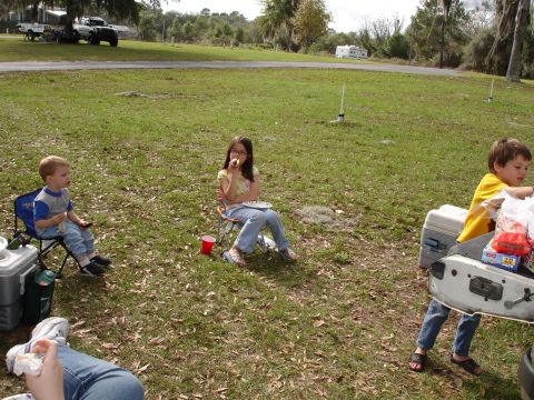 1989 Ford Bronco - A family enjoys a meal outdoors at a campsite, with vehicles parked nearby.