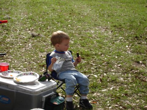 1989 Ford Bronco - A young child sits in a folding chair outdoors, holding a snack and a wrapper.