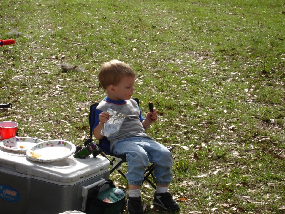 Child in a folding chair eating a snack next to a cooler