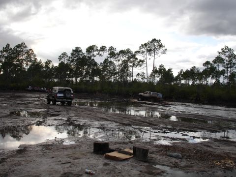 1989 Ford Bronco - Off-road vehicles traverse a challenging muddy landscape under a cloudy sky.