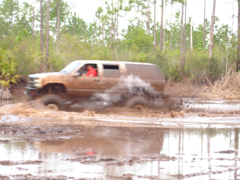 1989 Ford Bronco - This SUV is deep in the mud, kicking up a lot of spray as it drives through the water.