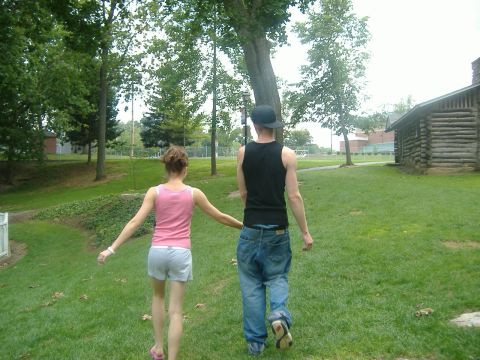 2001 BMW 3 Series - Couple walking through a park with trees and a log cabin in the background.