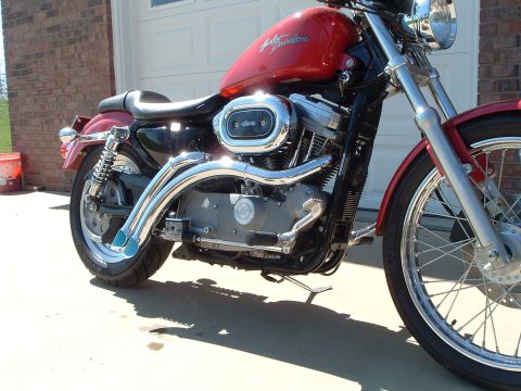 2002 Harley-Davidson Sportster Custom - A red Harley-Davidson motorcycle is parked in front of a garage, showing its engine and chrome details.