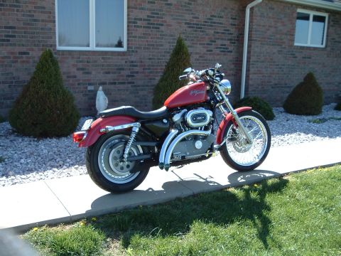 2002 Harley-Davidson Sportster Custom - A red 2002 Harley-Davidson Sportster Custom is parked on a sidewalk in front of a brick house.