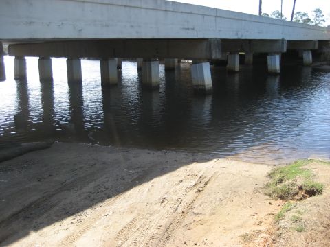 1986 Ford Bronco - Tire tracks mark a sandy ramp leading to the water beneath a concrete bridge.