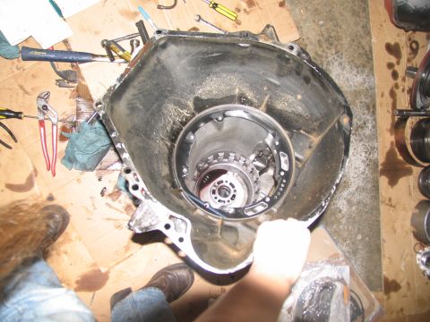 1978 Ford Bronco - A transmission housing is disassembled on a cardboard-covered floor, surrounded by tools and shop rags.