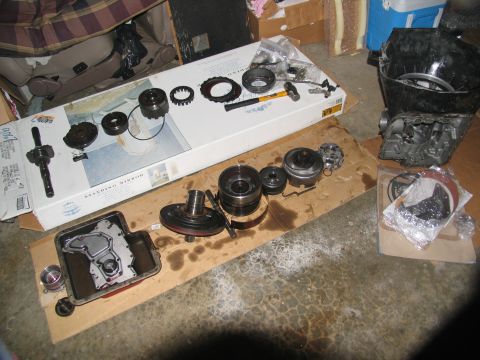 1978 Ford Bronco - Various transmission parts are spread out on the floor, some in a pan and others on a cardboard surface.