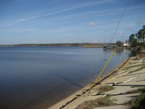 1986 Ford Bronco - Two fishing rods are set up on a concrete seawall overlooking a calm lake or bay.