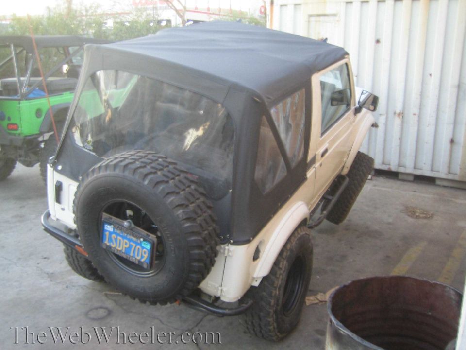 Tan Suzuki Samurai with a soft top and spare tire on the back. A green Jeep is parked behind it