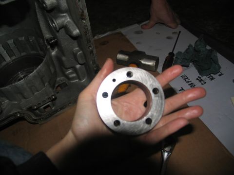 1978 Ford Bronco - A metal ring with bolt holes is held over a transmission during a rebuild.