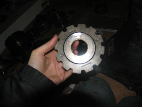 1978 Ford Bronco - A hand holds a metal gear, likely a transmission part, against a dark background with other components.