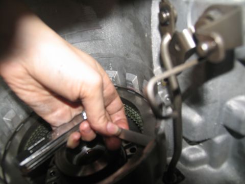 1978 Ford Bronco - Close-up of a hand working on a part inside a vehicle's transmission.