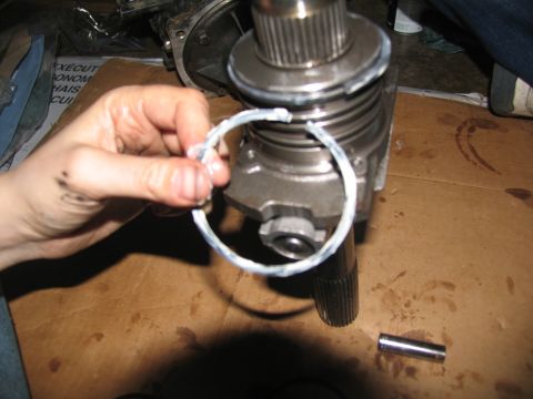 1978 Ford Bronco - A hand holds a metal ring with sealant over a transmission component, with a small pin on the cardboard surface.