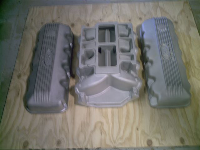 Two Ford valve covers and a center intake manifold on plywood