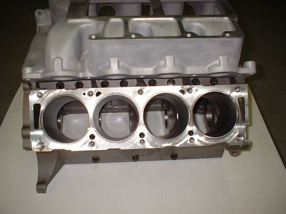 Bare aluminum V8 engine block showing four cylinder bores and machined deck