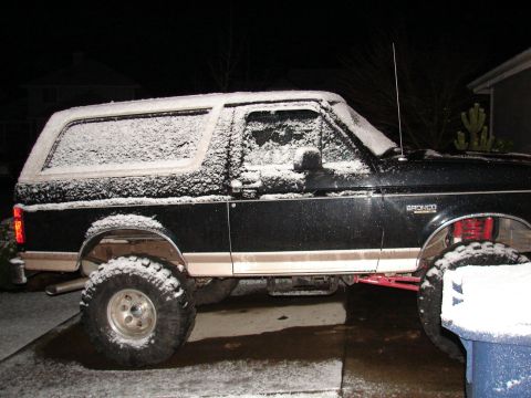 1996 Ford Bronco - A black 1996 Ford Bronco sits covered in snow, showing its lifted suspension and side profile.