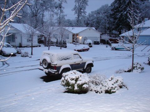 1996 Ford Bronco - A residential street is blanketed in snow, with several vehicles parked in driveways and on the street.