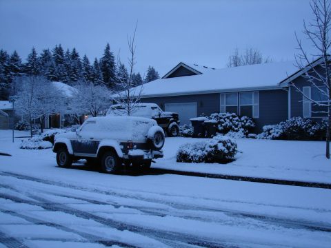 1996 Ford Bronco - A 1996 Ford Bronco and another SUV sit covered in snow on a quiet residential street during a winter snowfall.