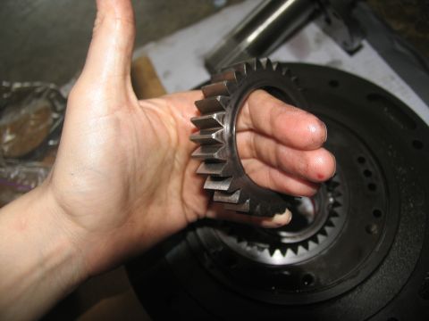 1978 Ford Bronco - A close-up view of a metal gear being held by a hand, with a larger component visible in the background.