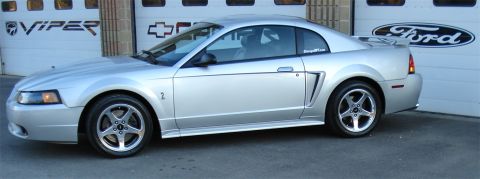 1998 Ford Taurus - Silver 1999 Ford Mustang coupe with racing stripes on hood, parked in front of a garage.