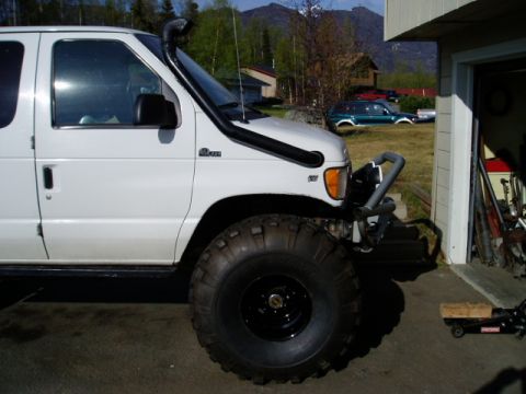 2000 Ford E350 - A white van is modified with a snorkel and large tires, parked in a driveway near a garage.