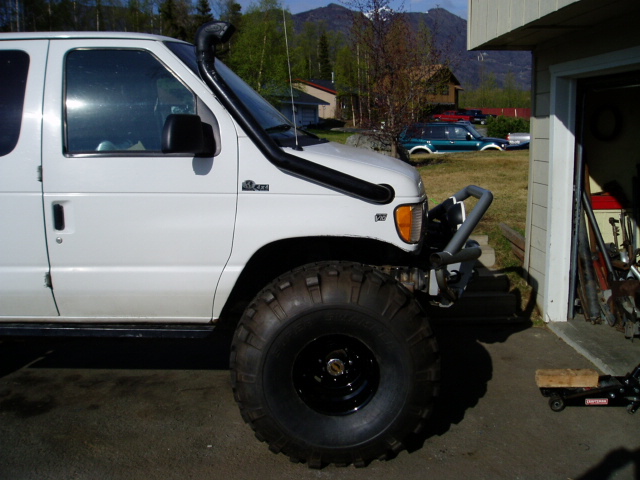 White van with snorkel and large off-road tires parked next to a garage