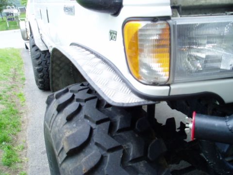2000 Ford E350 - A white van with oversized tires and custom fender trim is shown from a low front angle.