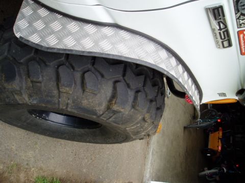 2000 Ford E350 - A white van features a large off-road tire and a diamond plate fender flare, with an E-450 Super Duty badge visible on the body.