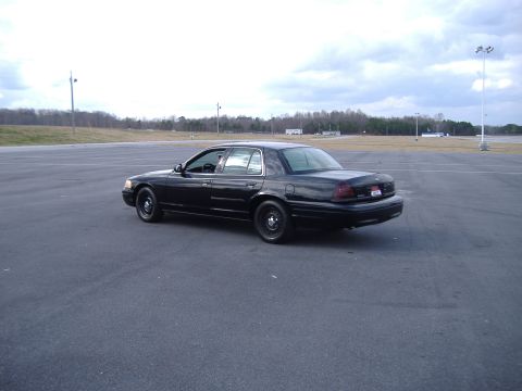 2001 Ford Crown Victoria - A black 2001 Ford Crown Victoria is shown from a three-quarter front angle on an open asphalt lot.