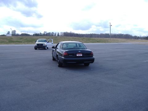 2001 Ford Crown Victoria - A black 2001 Ford Crown Victoria is parked on asphalt with a white truck in the distance.