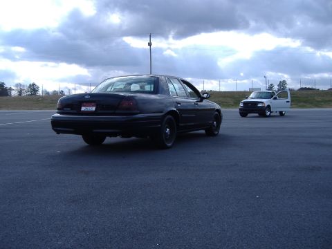 2001 Ford Crown Victoria - Two vehicles are visible in this outdoor shot, a black sedan and a white pickup truck.