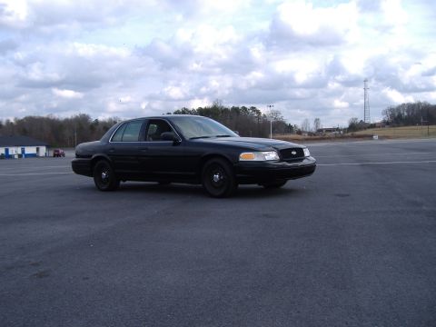 2001 Ford Crown Victoria - A black 2001 Ford Crown Victoria is parked on an asphalt lot under a cloudy sky.