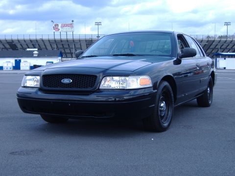 2001 Ford Crown Victoria - A black 2001 Ford Crown Victoria is parked in front of a racetrack grandstand.