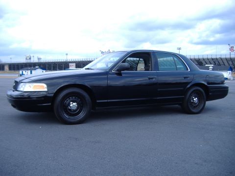 2001 Ford Crown Victoria - Side view of a black 2001 Ford Crown Victoria parked outdoors near a stadium.