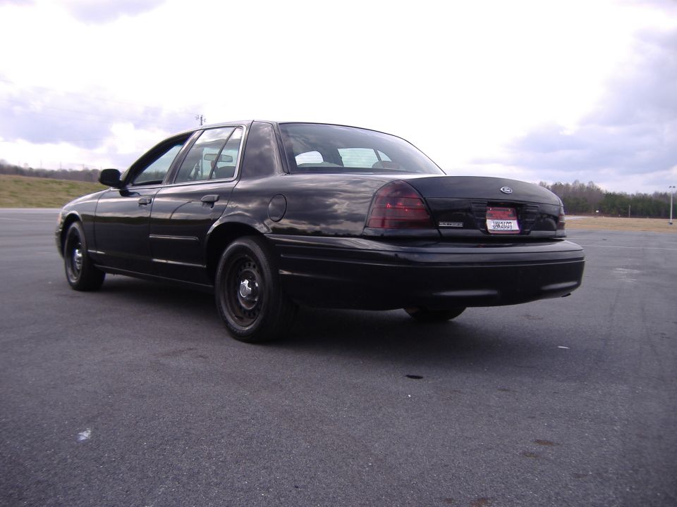 Black Ford Crown Victoria sedan on steel wheels, rear three-quarter view on asphalt lot