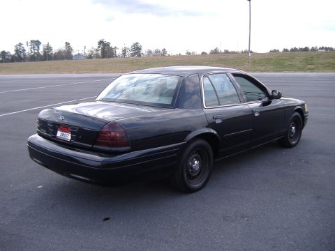 2001 Ford Crown Victoria - This black 2001 Ford Crown Victoria is viewed from the rear passenger side, parked in an empty lot.