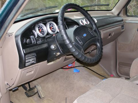 1993 Ford Bronco - The interior of a vehicle shows a tan dashboard, steering wheel, and aftermarket gauges, with visible wiring on the floor.