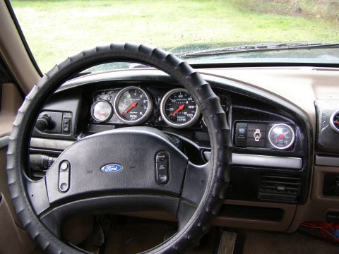 1993 Ford Bronco - The interior of a vehicle shows a dashboard with a Ford steering wheel and several aftermarket gauges.