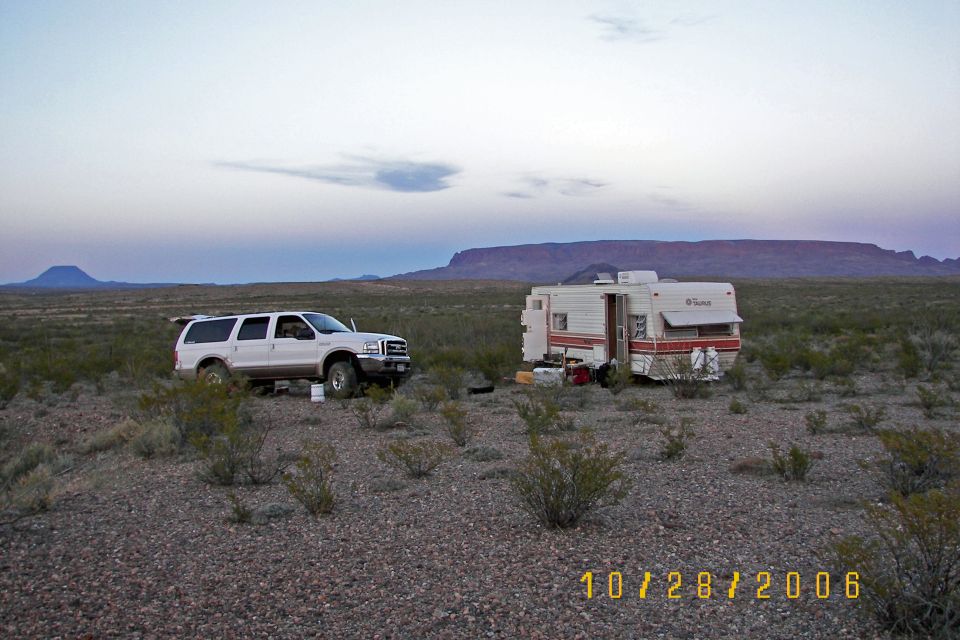 White Ford Excursion and travel trailer camped in open desert with mesas in the distance at dusk