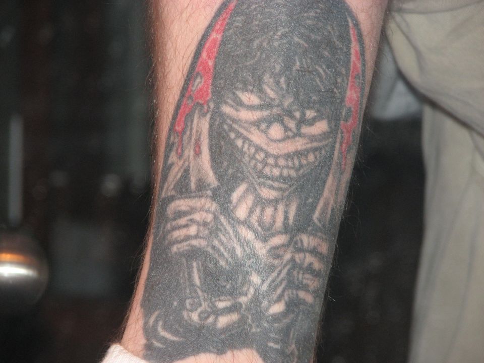 Close-up forearm tattoo of a grinning hooded skeleton with red drips