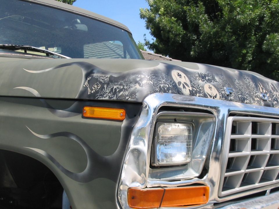 Front corner of green Ford Bronco with airbrushed skulls and flames, chrome grille and square headlight