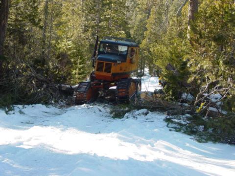 1986 Ford Bronco - A tracked vehicle operates in a snowy woodland environment, clearing felled trees.
